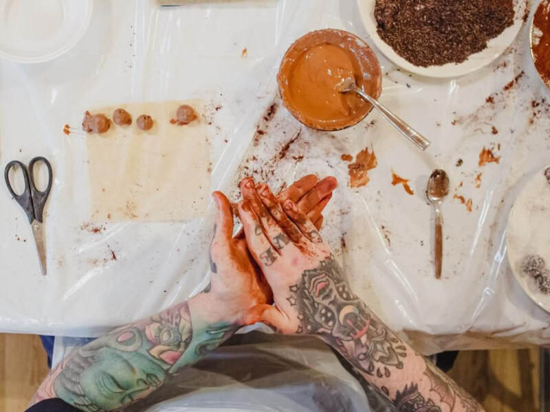 Aerial shot of tattooed hands covered in chocolate, at a table with chocolate making ingredients